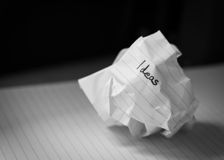 Zusammengeknülltes Papier mit der Aufschrift "Ideen" auf einem linierten Blatt bei Namensentwicklung.